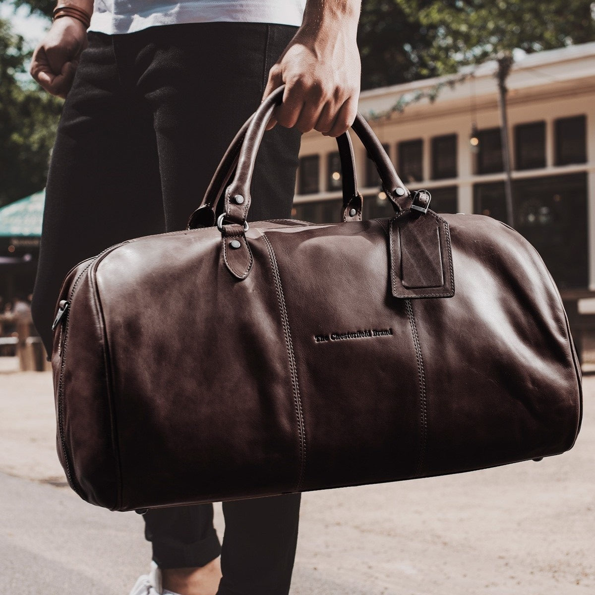 Mann trägt Chesterfield Weekender William Braun an den Griffen – Lifestyle-Aufnahme urban, schwarze Jeans