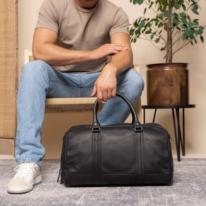 Mann mit The Chesterfield Brand Perth Schwarz – Lifestyle-Aufnahme sitzend, Jeans und Sneaker, Innenraum